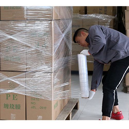 En person som säkrar paket på en pall med sträckfilm för säker möbelfrakt.