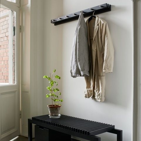 Ljus hall med klädhängare, jackor, växt och svart sittbänk